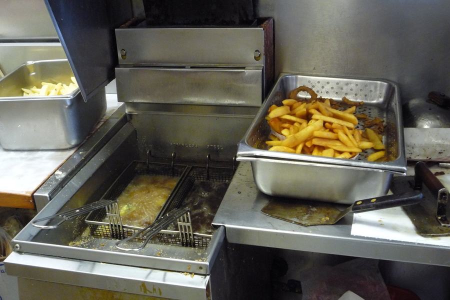 Restaurant fryer with golden oil and baskets, a pan of fries and onion rings resting on top