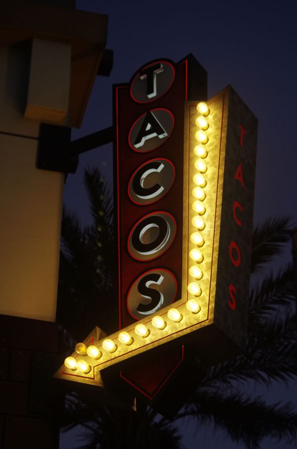 Lit tacos marquee sign at dusk with palm trees behind