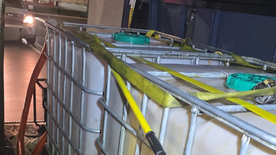 Two totes of used cooking oil held down with yellow ratchet straps inside a van at night